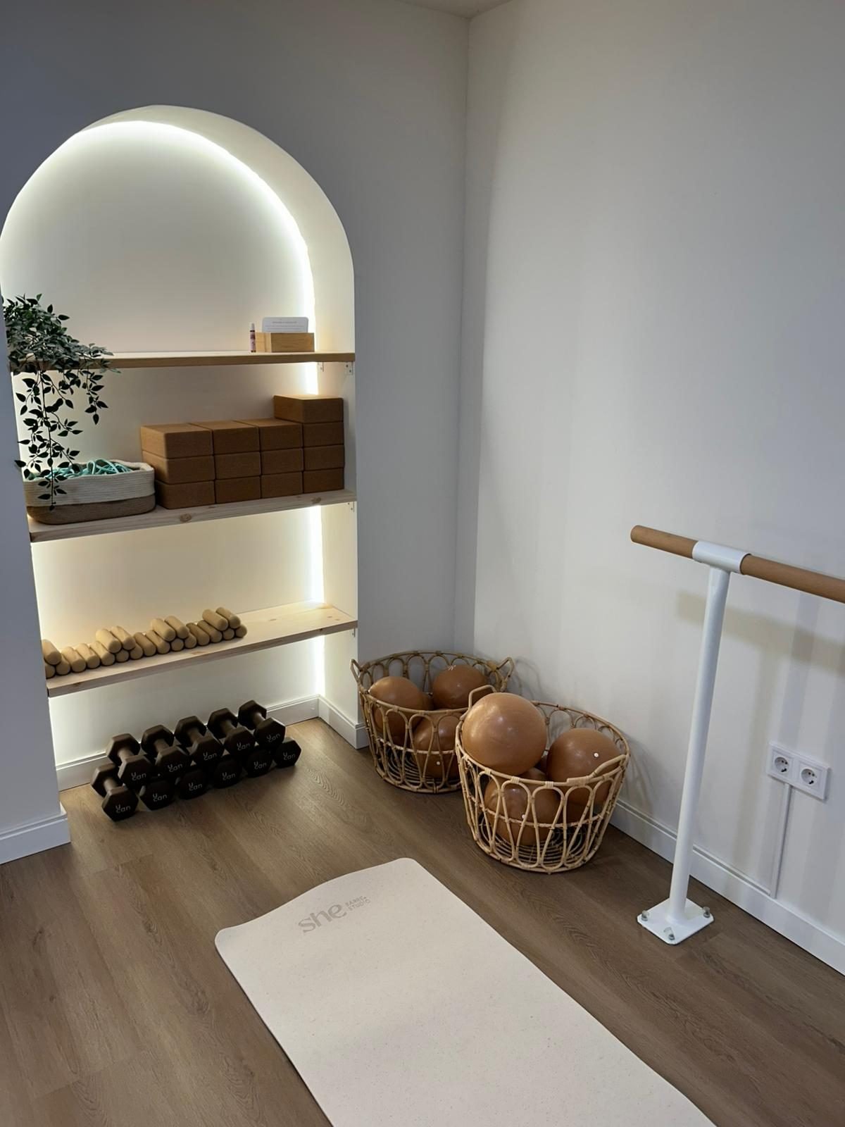 Rincón de la sala con barra, esterilla, mancuernas y cestas con pelotas de pilates